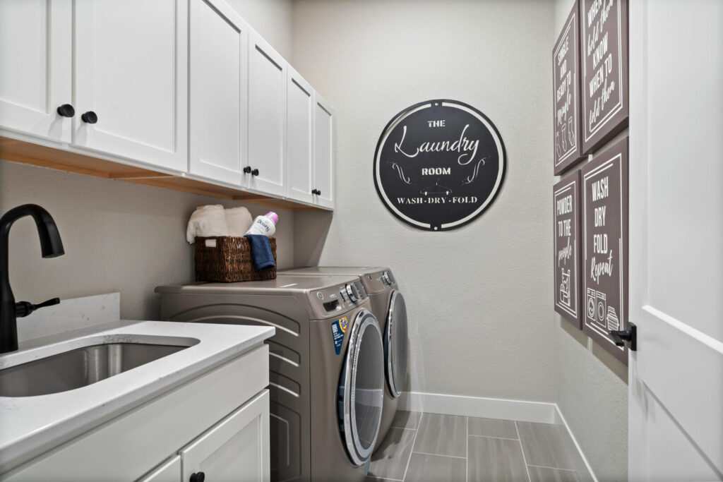 Laundry room with front-load washer and dryer, white cabinets, and decorative wall signs.