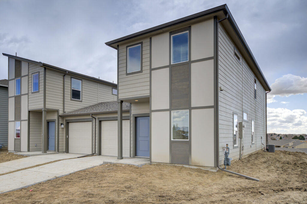 Modern two-story townhouse exterior with attached garage and blue front door under cloudy sky.
