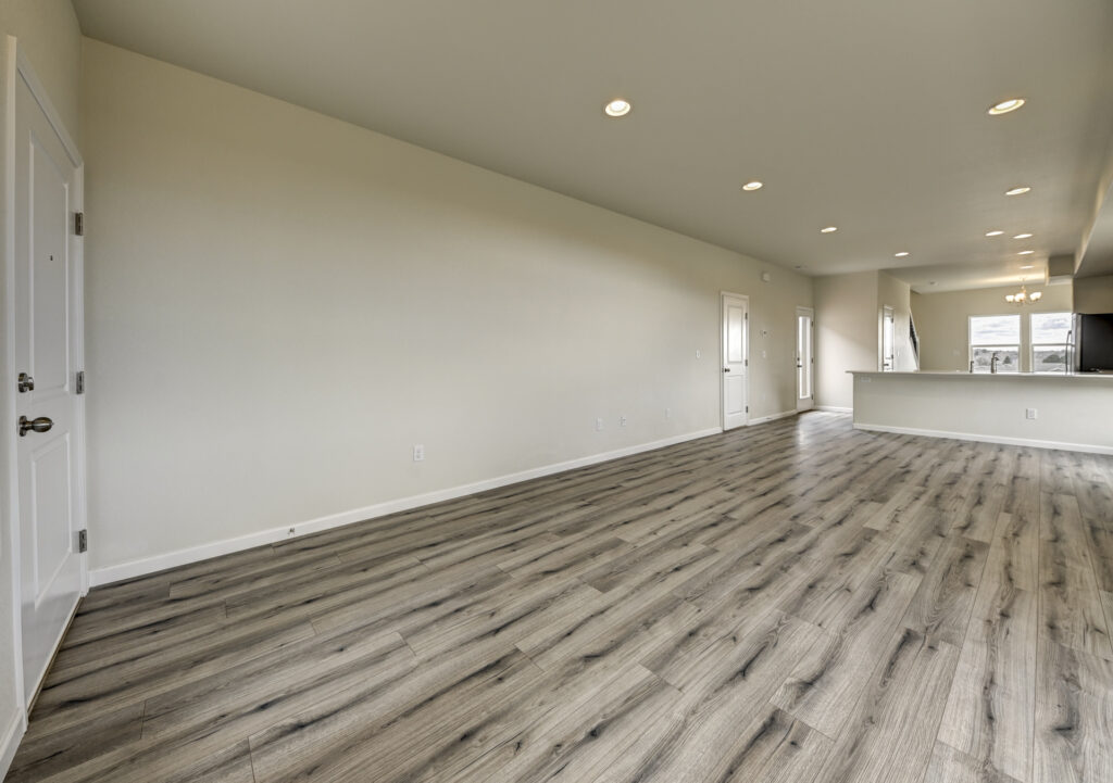 Open interior room with wood-look floor, recessed lights, and a doorway to the kitchen.