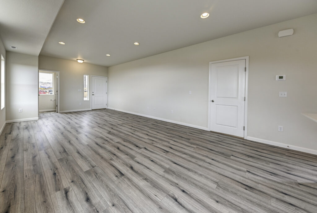 Long empty room with gray plank flooring, recessed lights, and a white interior door on the side wall.