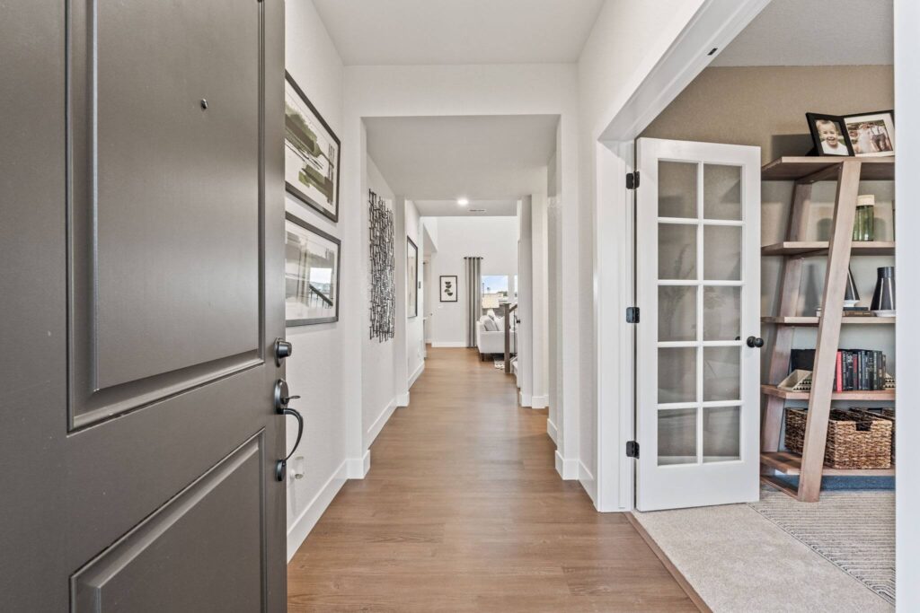 Open front door looking down a hallway with wood-look flooring and a room with French doors.