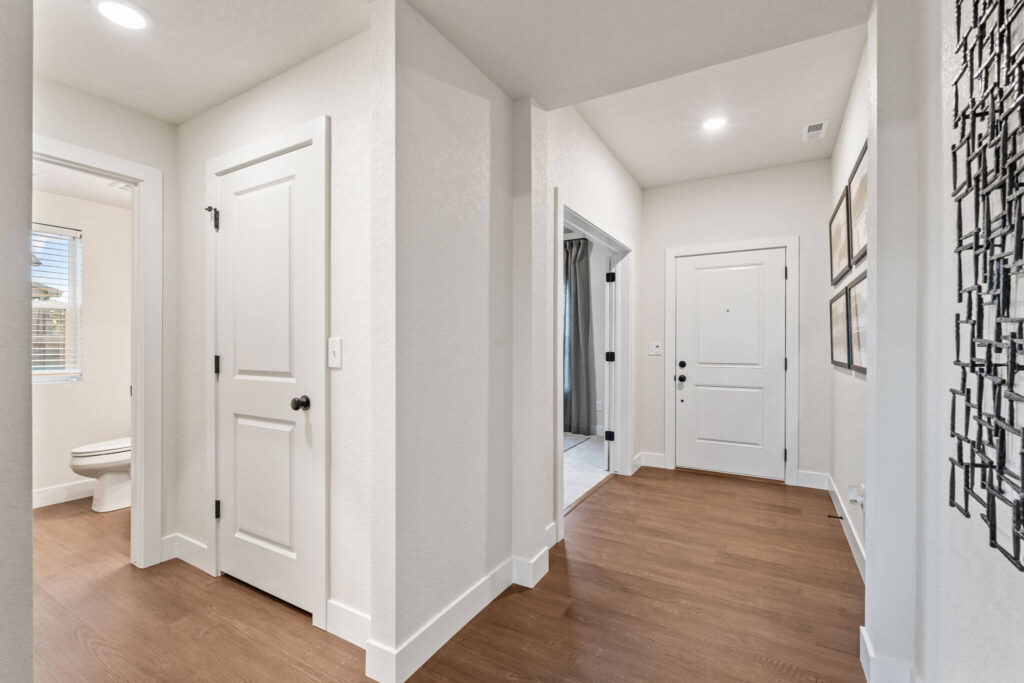 Bright entry hall with white doors, wood-look flooring, and simple wall art.