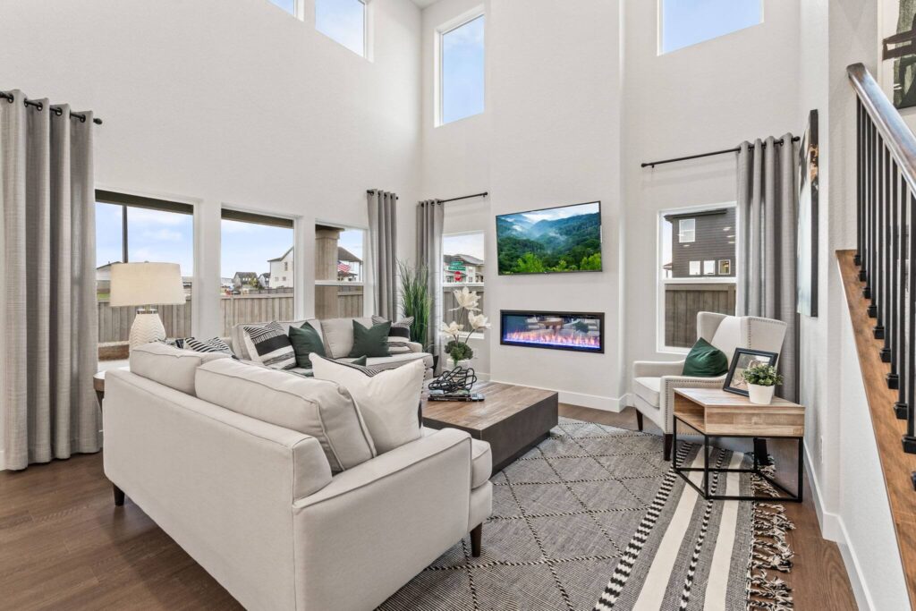 Bright living room with paired sofas, wall-mounted TV, linear fireplace, and tall windows.