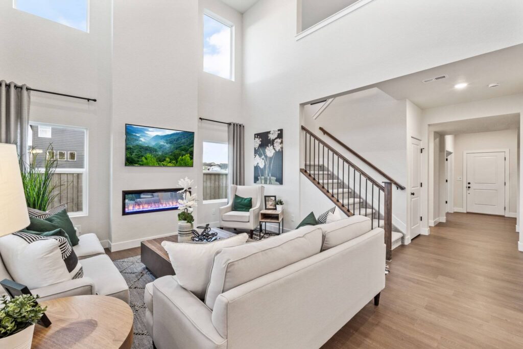Two-story living room with high windows, mounted TV and seating arranged around a fireplace.