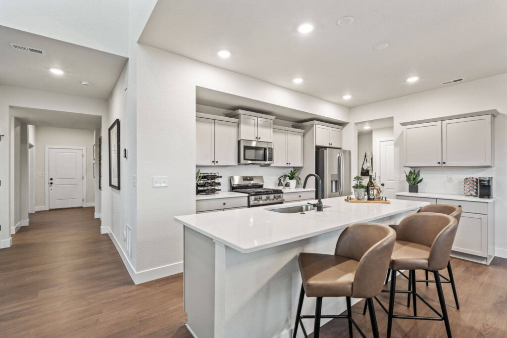 Kitchen island with sink and three counter-height stools, view into hallway and appliances.