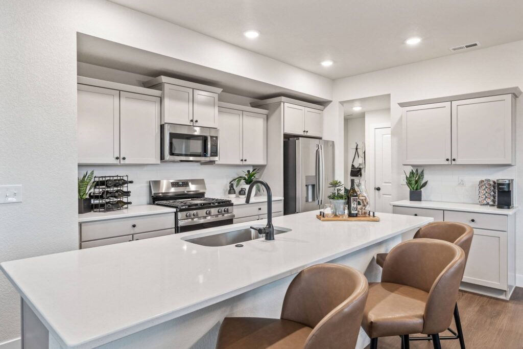 Bright open kitchen with a long white island, sink, stainless appliances, and three tan bar stools.