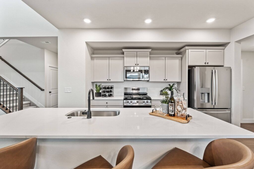 View of a white kitchen island and sink with stainless stove and refrigerator beyond.