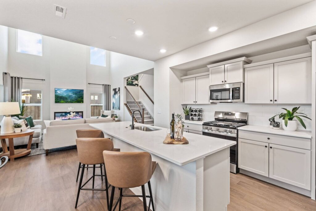 Open-concept kitchen flowing into a two-story living room with tall windows and fireplace.