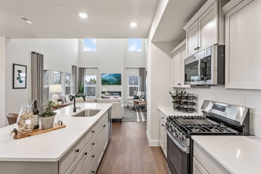 Bright open kitchen with large island, stainless range and sink, looking toward living area.