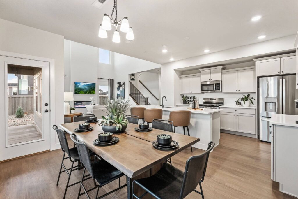 Open-plan dining area with wooden table, black chairs, island seating, and white kitchen in background.