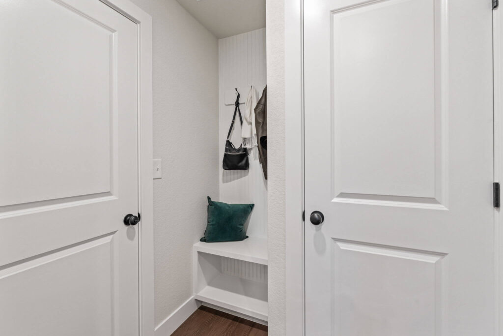 Small entry alcove with built-in bench, hooks above, and a green throw pillow between two white doors.