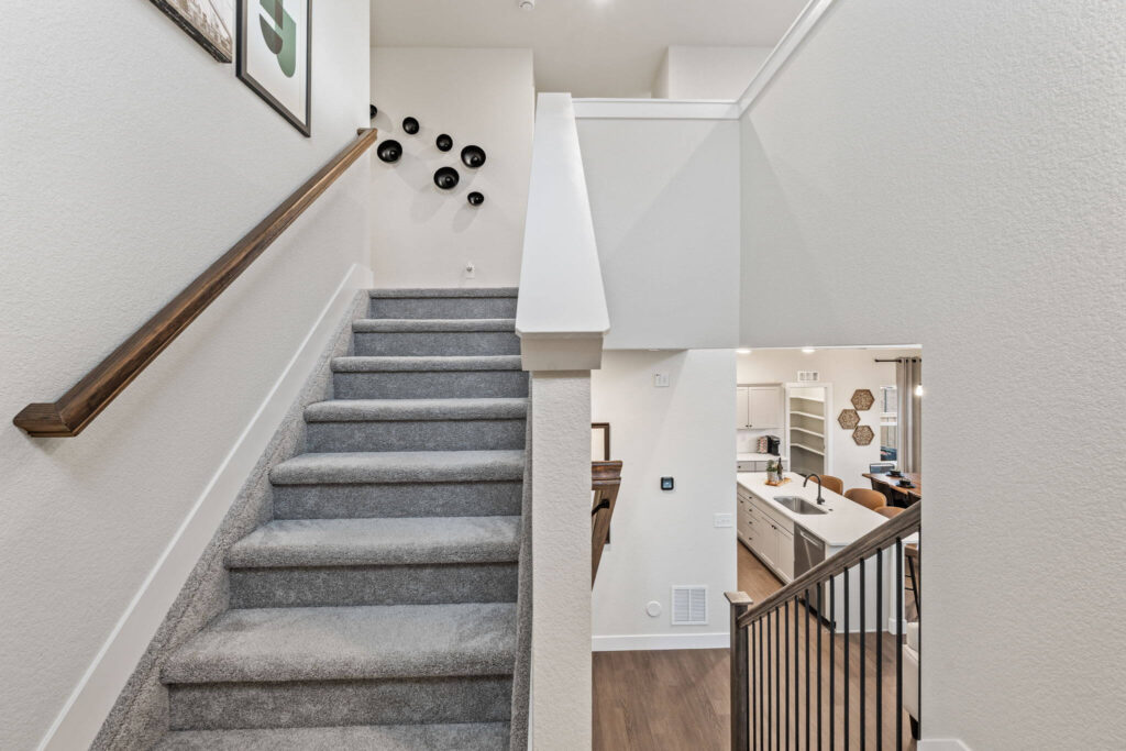 Carpeted staircase and landing with wooden handrail overlooking the kitchen and living area below.