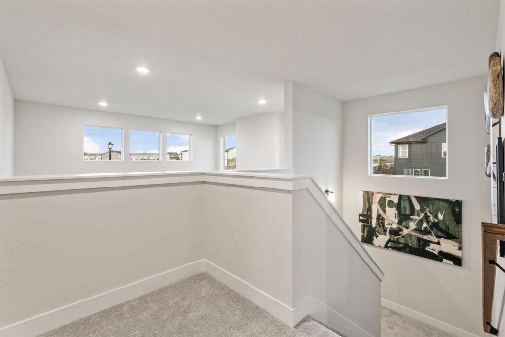 Top of a carpeted stair landing with white half-walls and multiple windows letting in daylight.