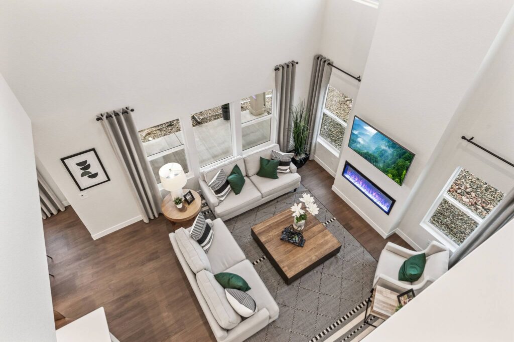 View down into a bright living room with two sofas, large windows and a wall-mounted TV and electric fireplace.