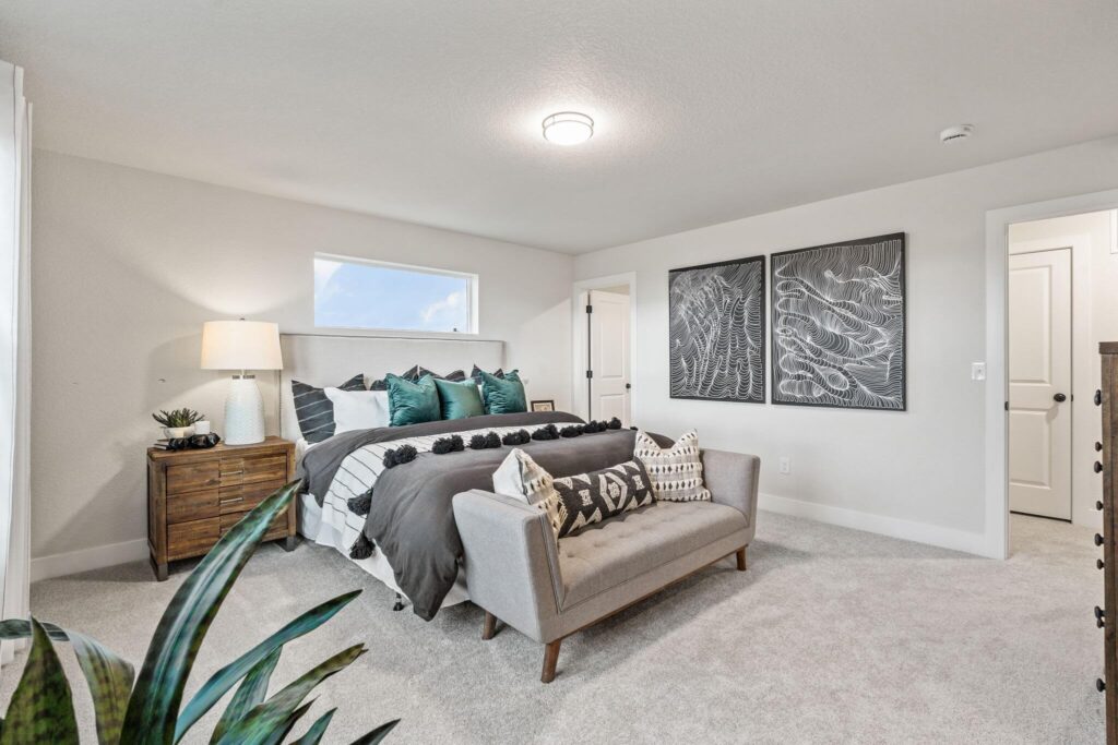 Bright bedroom with upholstered bed, small sofa at foot, wooden nightstand and wall art.