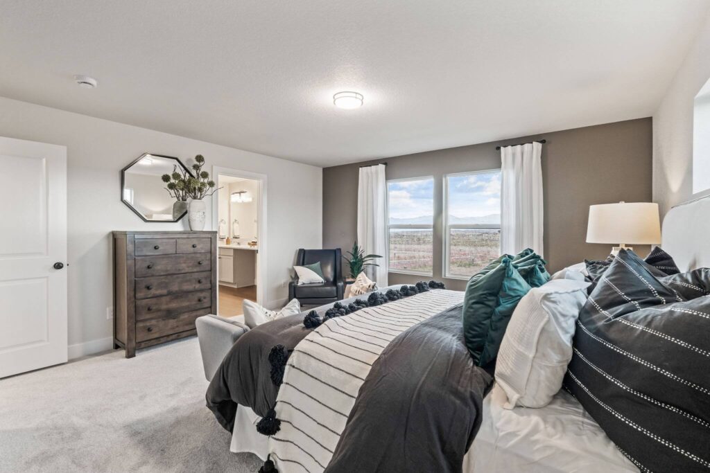 Bedroom with large window, bed in foreground, dresser and armchair near the window.