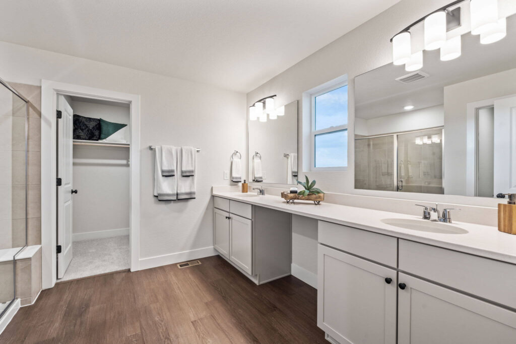 Bright bathroom with long dual-sink vanity, large mirror, and walk-in closet doorway.