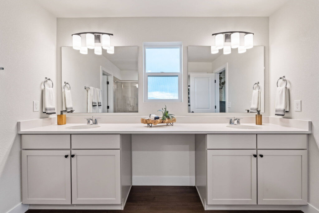Double-sink vanity under two mirrors with a small central window and modern light fixtures.