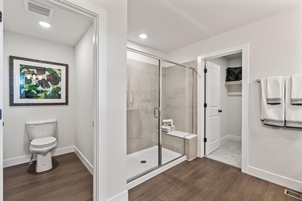Bathroom view showing a toilet alcove, glass shower enclosure, and open closet door.