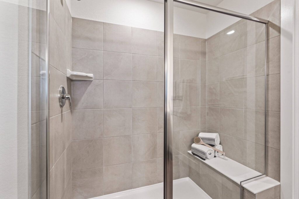 Tiled walk-in shower with glass sliding door and built-in bench holding rolled towels.