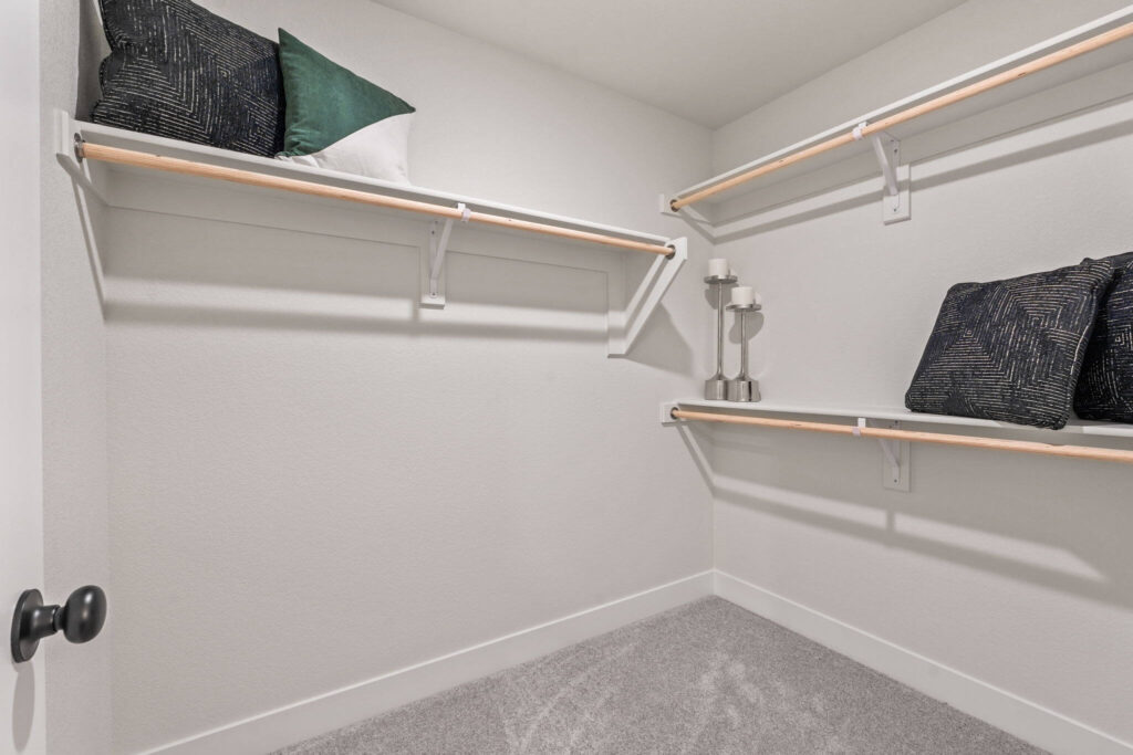 Empty walk-in closet with white walls, carpeted floor and wood-and-white closet rods.