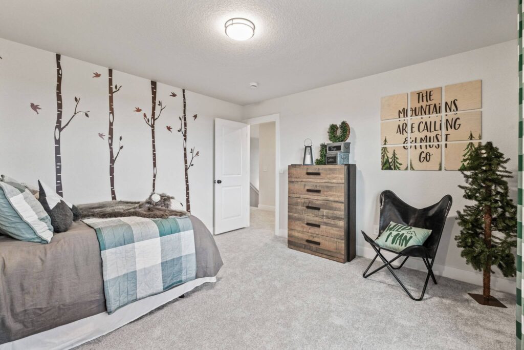 Bedroom with rustic dresser, accent chair, tree decals on wall, and decorative sign.