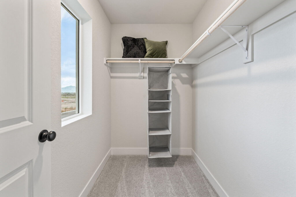 Small walk-in closet with hanging rods, shelf organizer and a window letting in natural light.