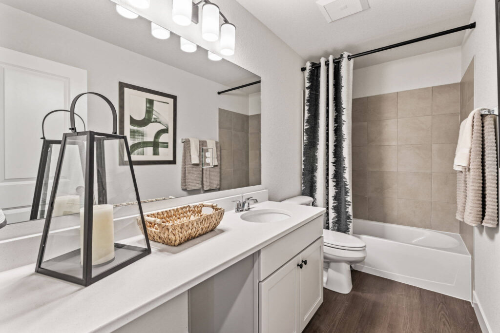 Bathroom vanity with double sink, mirror, tub-shower and decorative candle lantern.
