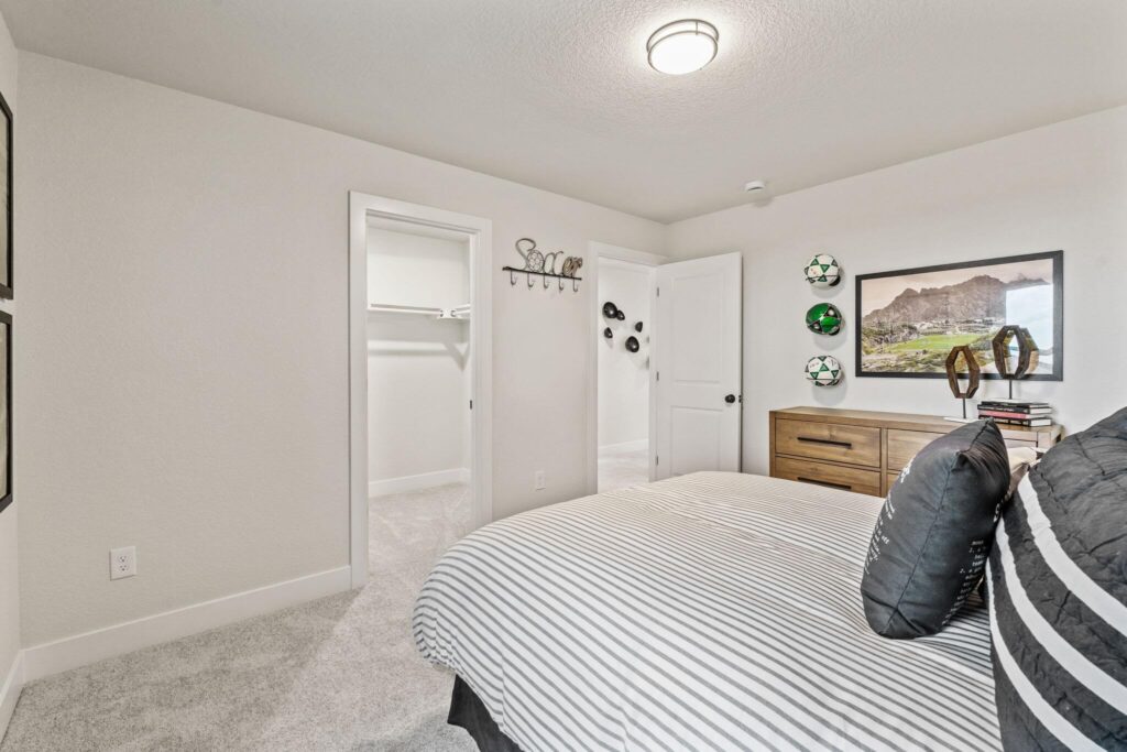 Bright bedroom with striped bed, light carpet, open closet and dresser against a wall.