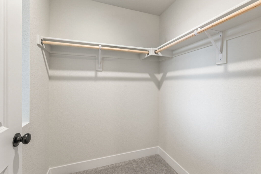 Small empty walk-in closet with two hanging rods and light carpet.