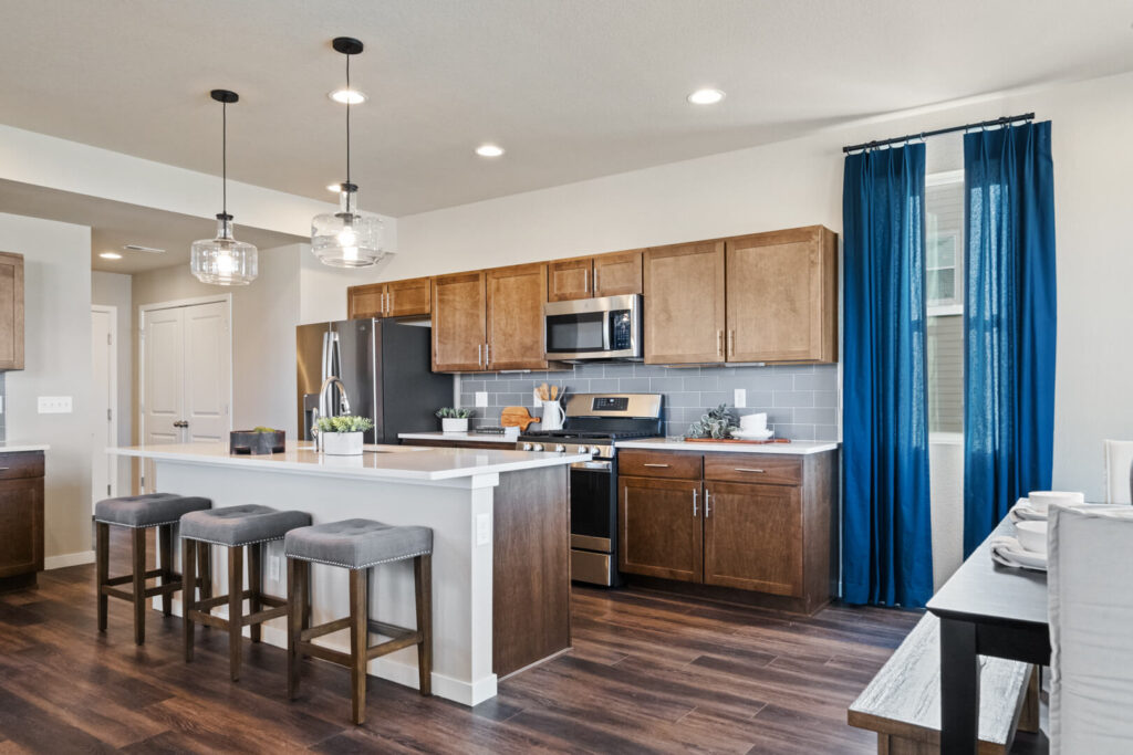 Bright open kitchen with island, three bar stools, wood cabinets and blue curtains.