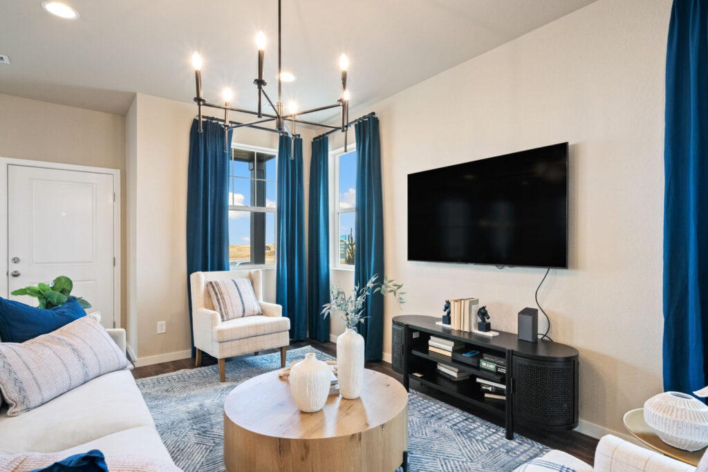 Bright living room with wall-mounted TV, round coffee table, blue curtains, and armchair.
