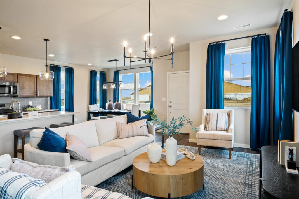 Open-concept living and dining area with sofa, kitchen island, pendant lights, and blue curtains.
