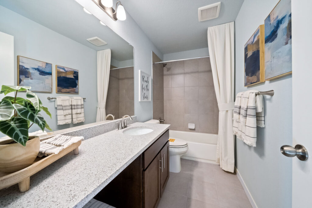 Bathroom with single-sink vanity, large mirror, tub-shower with curtain, and neutral tile flooring.
