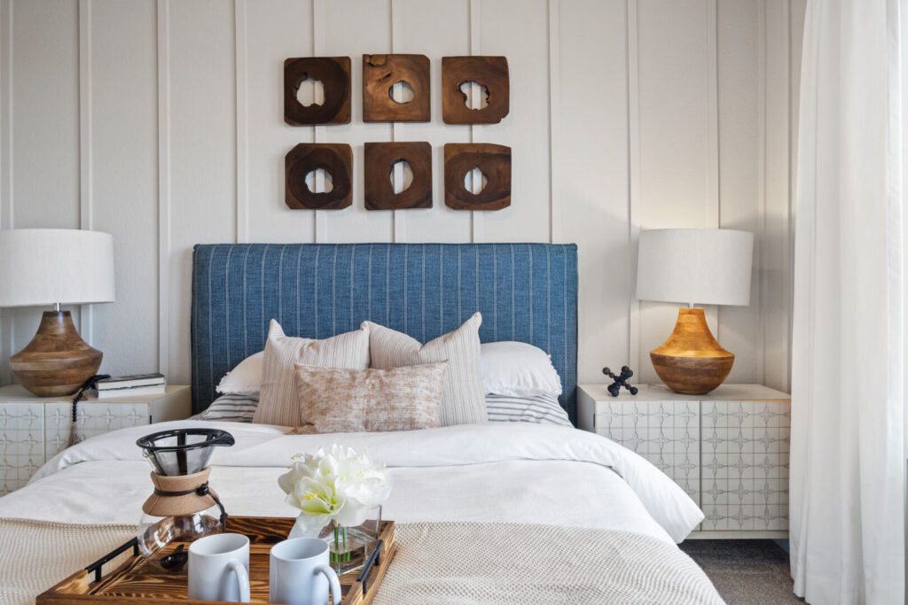 Close view of a made bed with striped blue headboard, matching nightstands and lamps, and decorative tray.