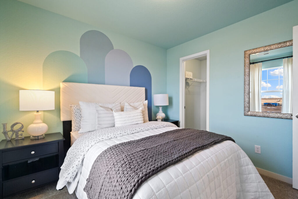 Teal bedroom seen from foot of bed, decorative arch mural above headboard and mirror on wall.