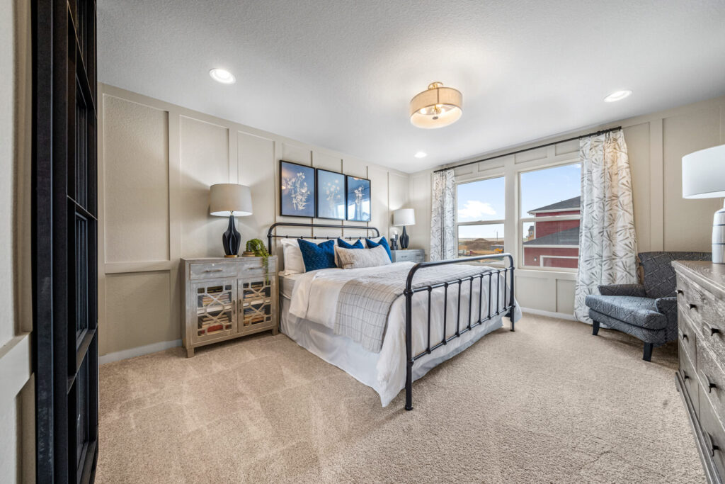 Spacious master-style bedroom with iron bedframe, carpeted floor and large window to outside.