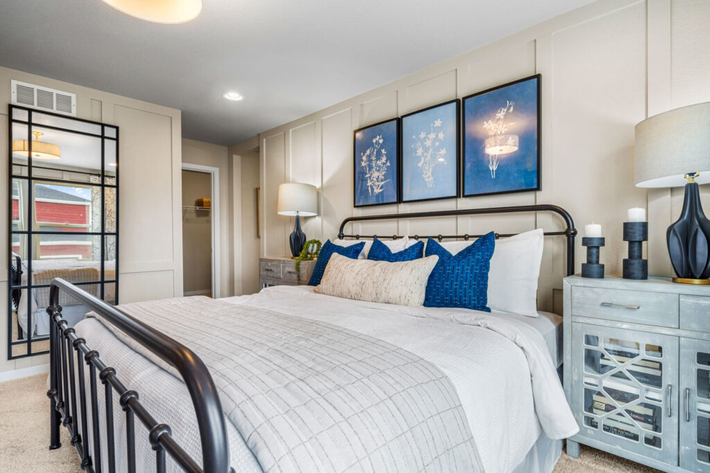 King-size bed with metal frame, blue accent pillows and mirrored nightstand in a bright bedroom.