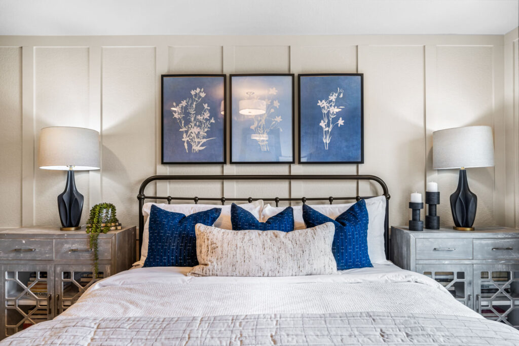 Headboard view of bed with blue decorative pillows and three botanical prints on paneled wall.