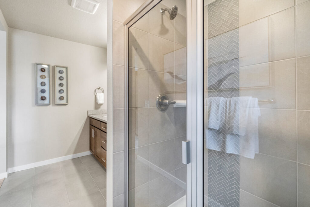Tiled walk-in shower with glass door and bathroom vanity visible through the doorway.