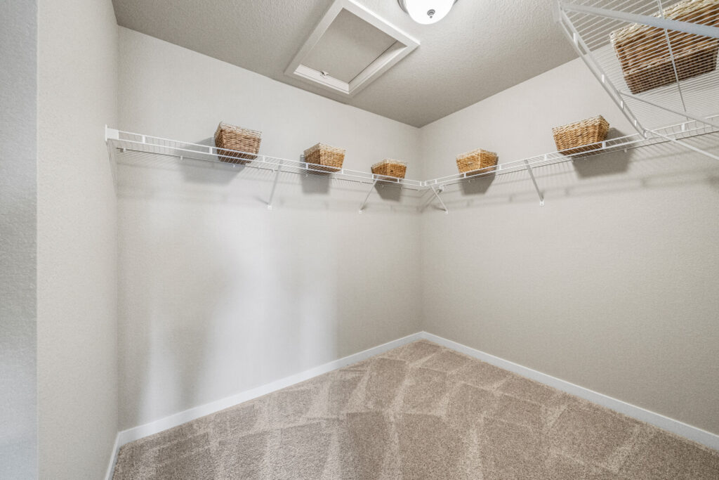 Empty carpeted walk-in closet with wire shelving and woven storage baskets on upper shelf.