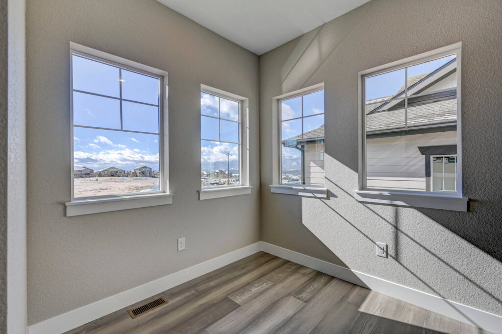 Bright corner room with three tall windows letting in sunlight onto wood-look floors.