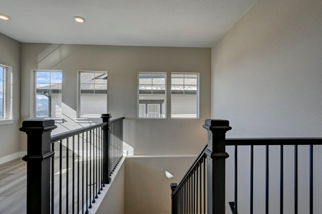 Staircase landing with black newel posts and three upper windows letting in daylight.