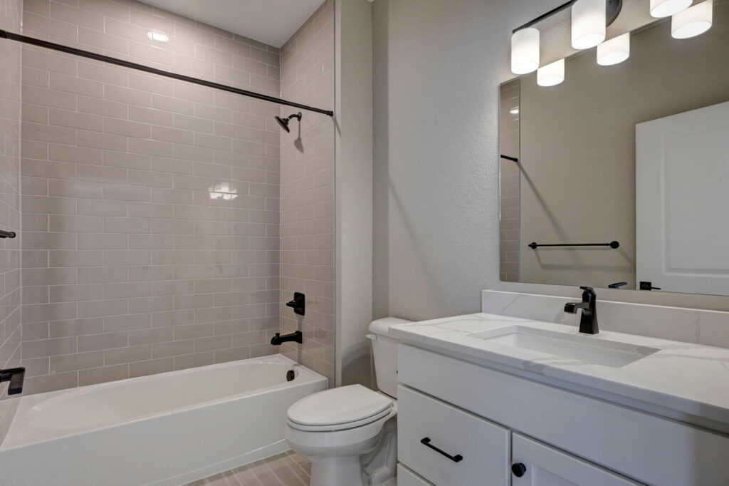 Bathroom with white vanity, mirror, bathtub and tiled shower surround in neutral tones.