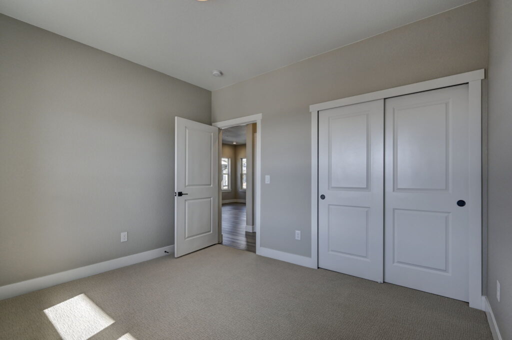 Empty carpeted room with closed double-closet doors and an open door leading to a hallway.
