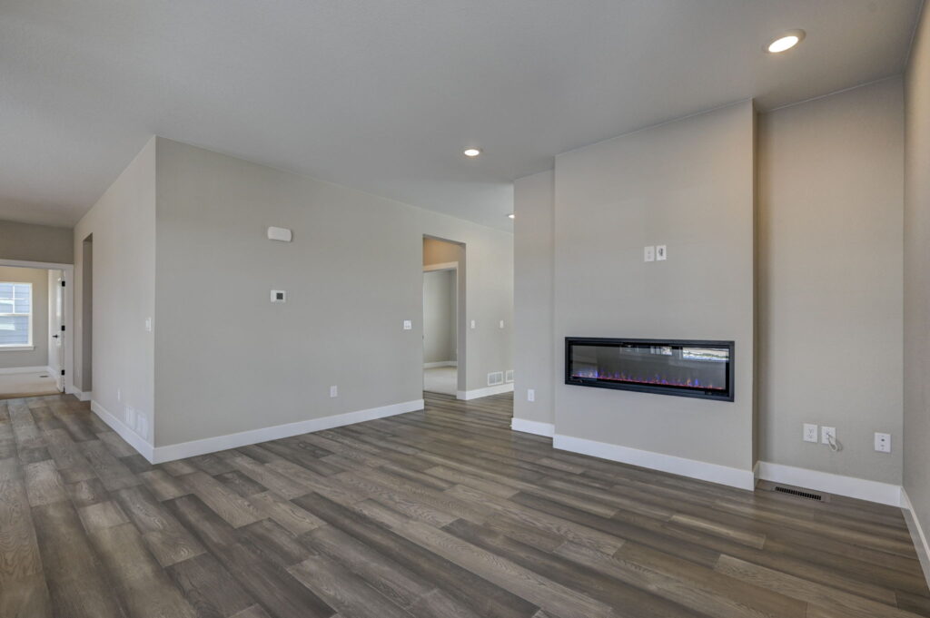 Empty open living area with wall-mounted linear electric fireplace and gray wood-look flooring.