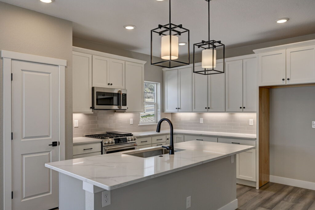 Kitchen island and countertop with black faucet, white cabinets, and pendant lighting.