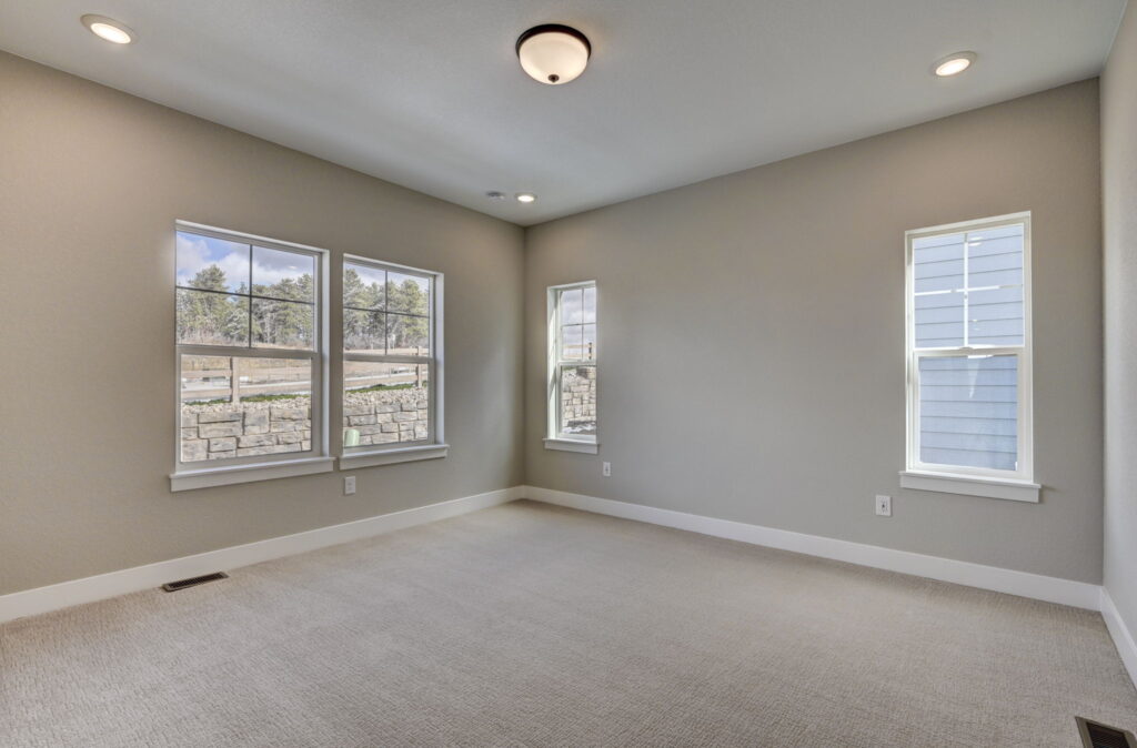 Empty carpeted room with three windows and neutral paint, recessed and ceiling lighting.