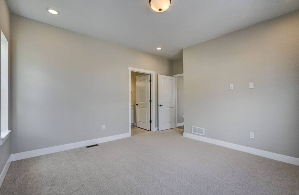 Empty carpeted room with closed white door and recessed ceiling lights, neutral decor.