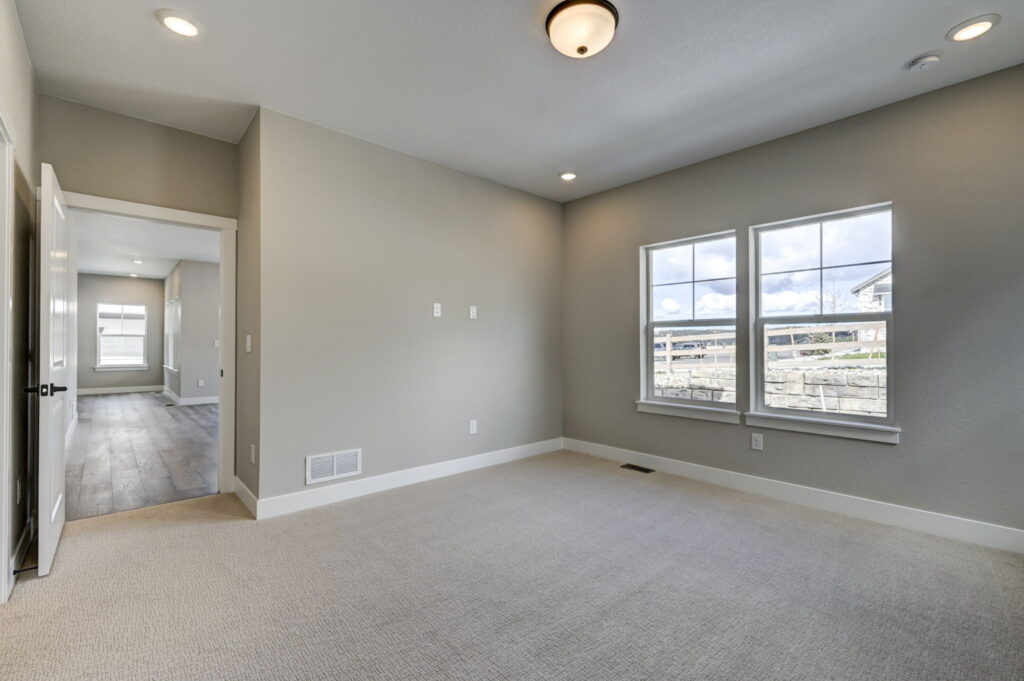 Light-filled carpeted room with two windows and open doorway leading to a hallway with wood-look floors.